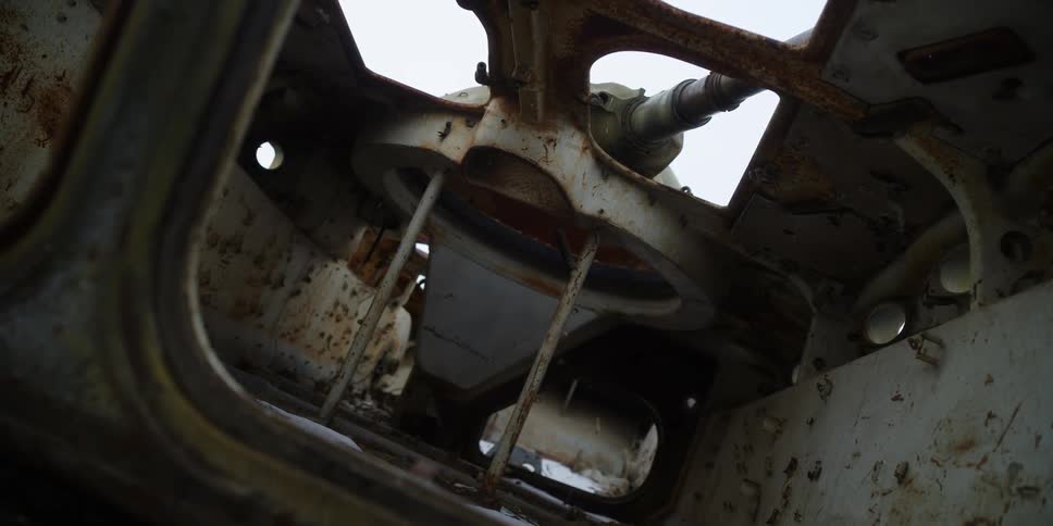 Inside an abandoned tank with rusted metal with the sky and clouds above