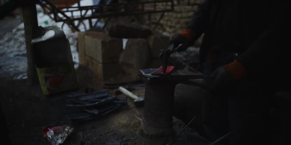 Two people shaping metal with a spike and hammer