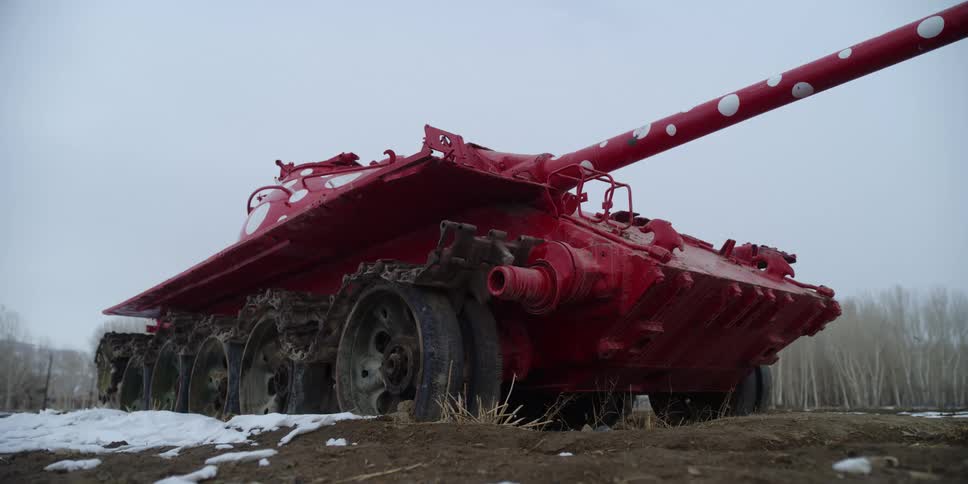 A tank on a field with trees the sky and clouds in the background