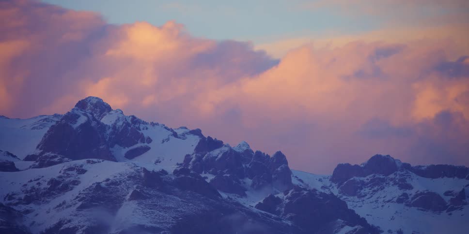 A mountain range covered in snow with the sky and clouds in the background