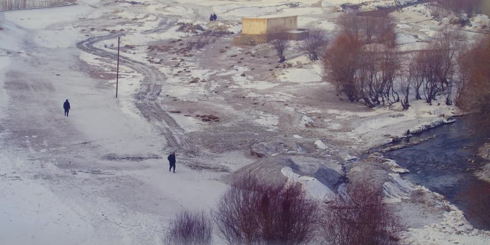 People walk across snow covered ground toward river