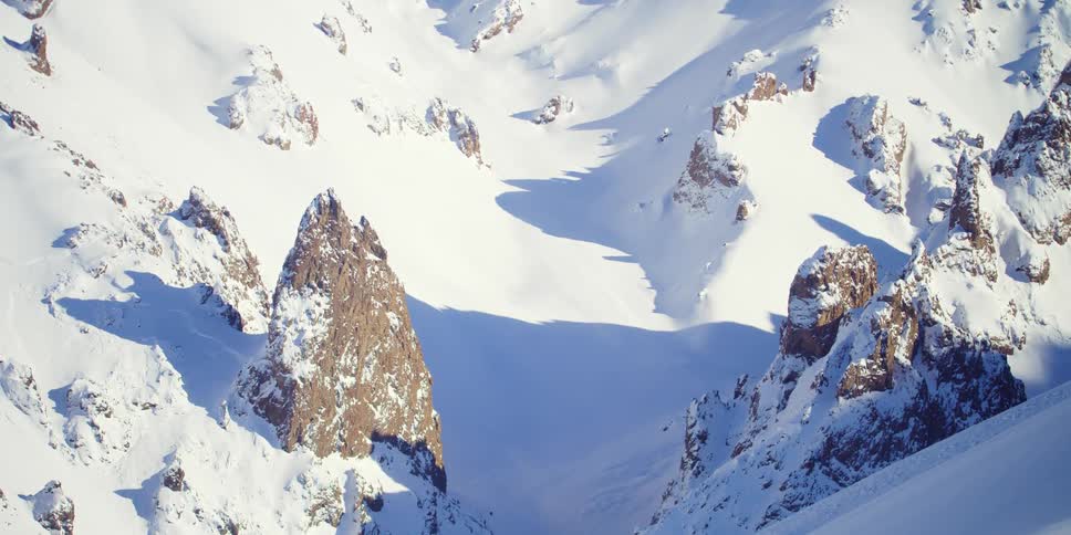 Rock formations and boulders stick up through the snow on a mountain slope during the day