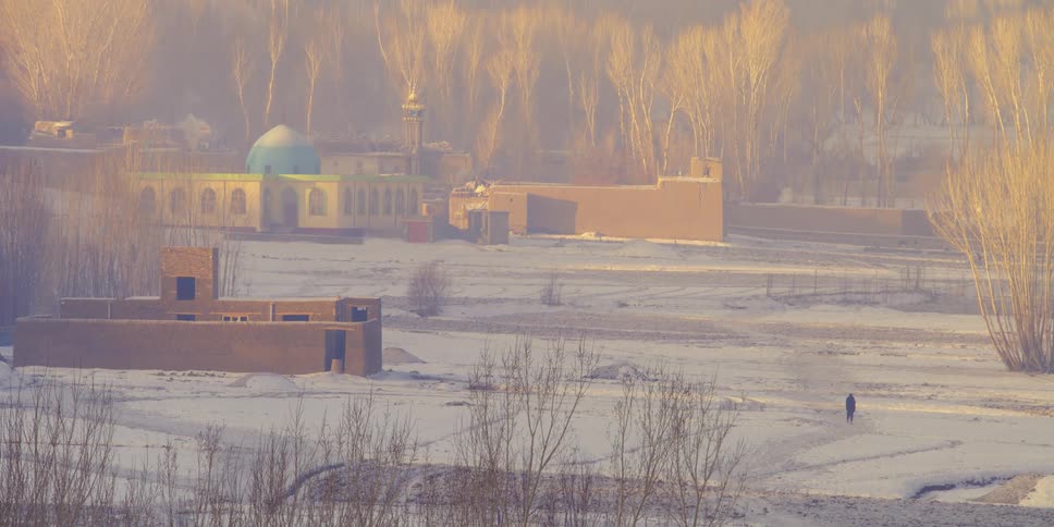 A person walks across a snowy field towards a temple