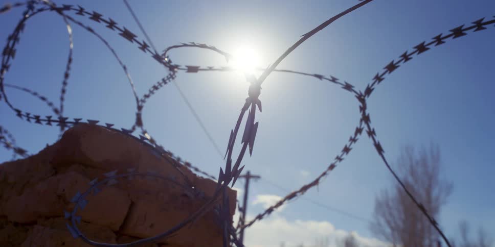 A wall with barbed wire with trees the sky and clouds in the background