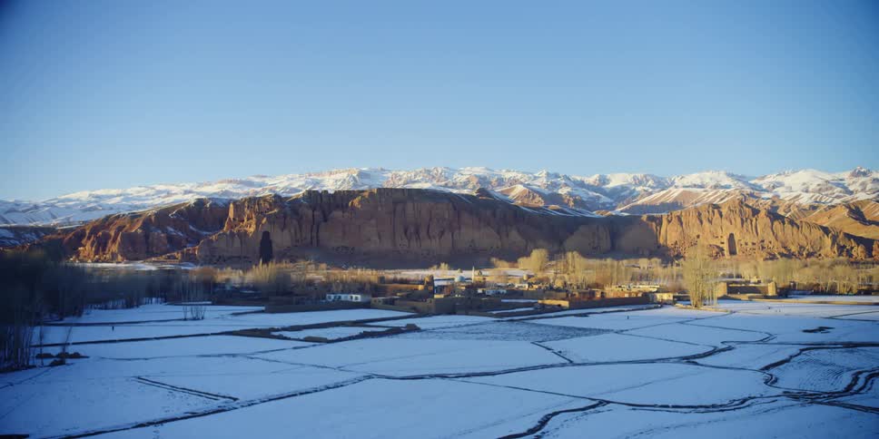 Snow covers the peaks of a canyon where primitive homes are carved into the side