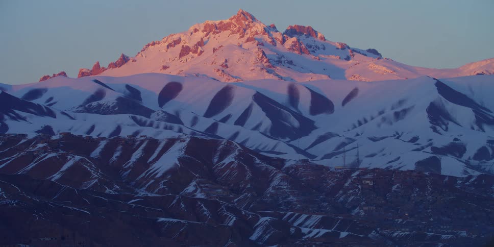Orange tint of the sunset over the snow covered mountain peaks