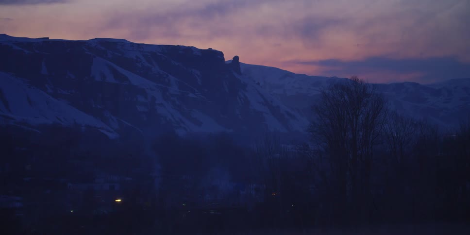 Cars travel along a road at the bottom of a large mountain ridge