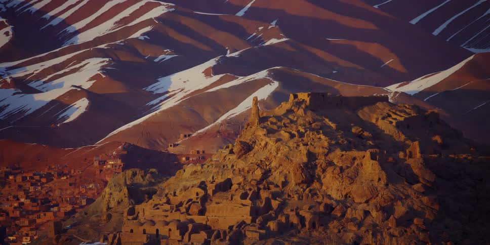 Landscape view of a rock formation in front of sandy hills with snow on them