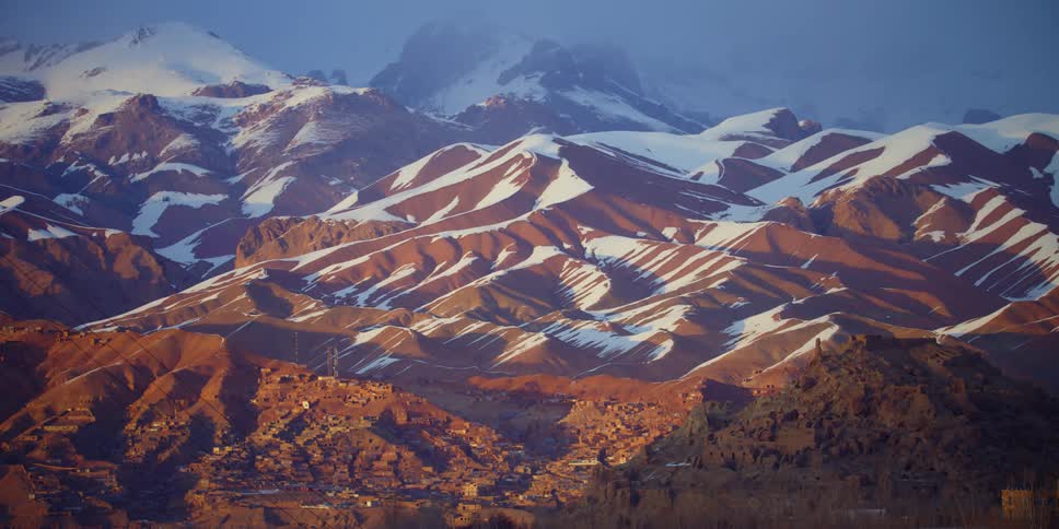 The sun is setting above the snow covered mountains