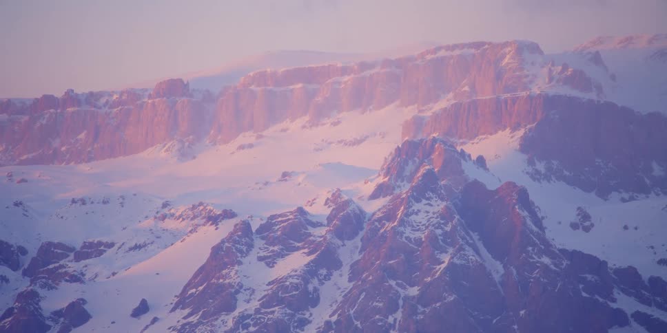 A rocky snow covered mountain slope on a foggy evening