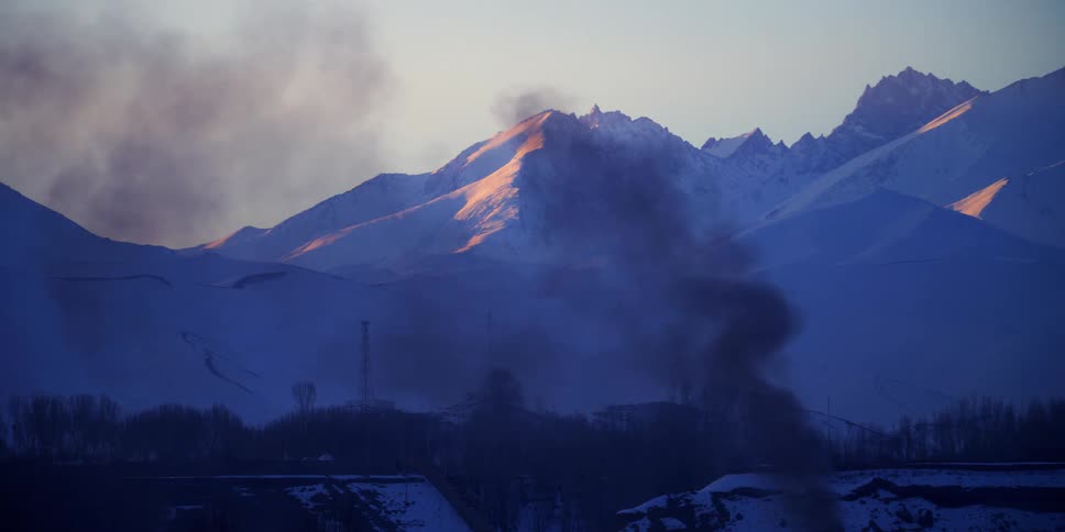 Black smoke rises from a neighborhood in front of a mountain range