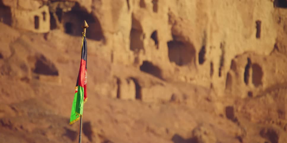 A flag waving in the wind with a cliff in the background