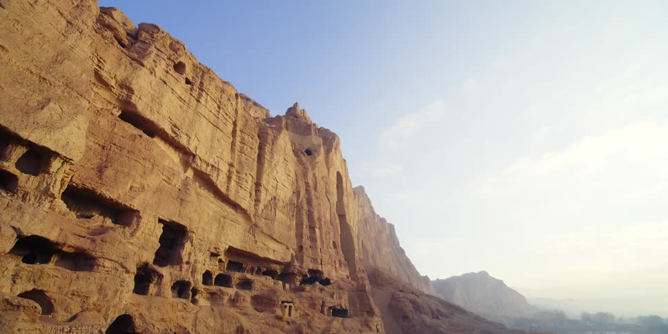 Cave dwellings are scattered on cliff side as fog covers nearby mountains