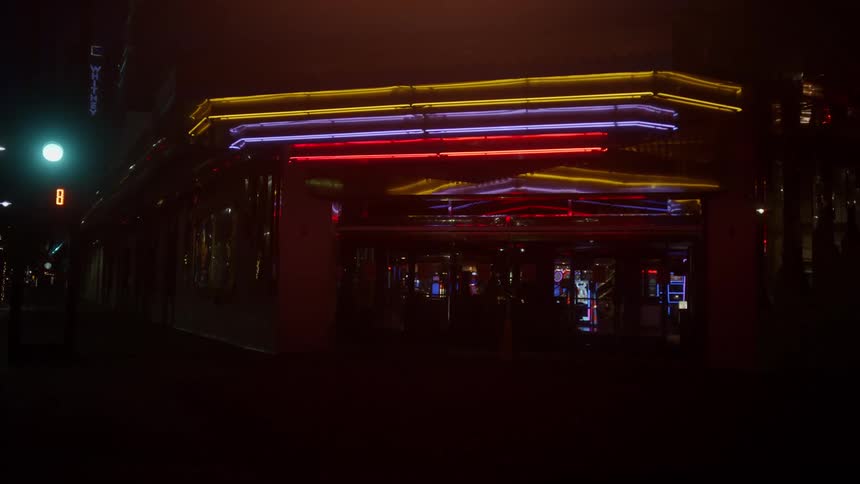 A dark building with lights above the doorway on the corner of a street in a metropolis at night