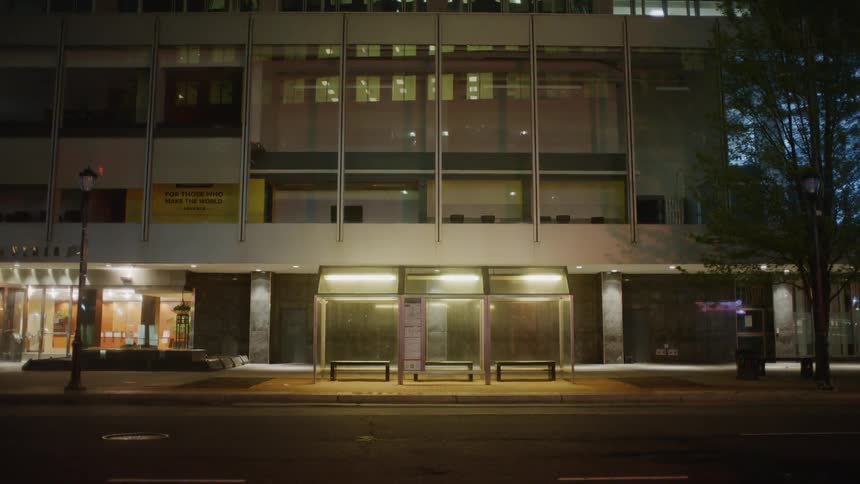 A bus stop in front of a tall building in the evening