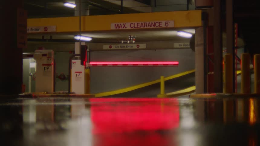 An illuminated boom gate bars entrance to a parking garage on a rainy night
