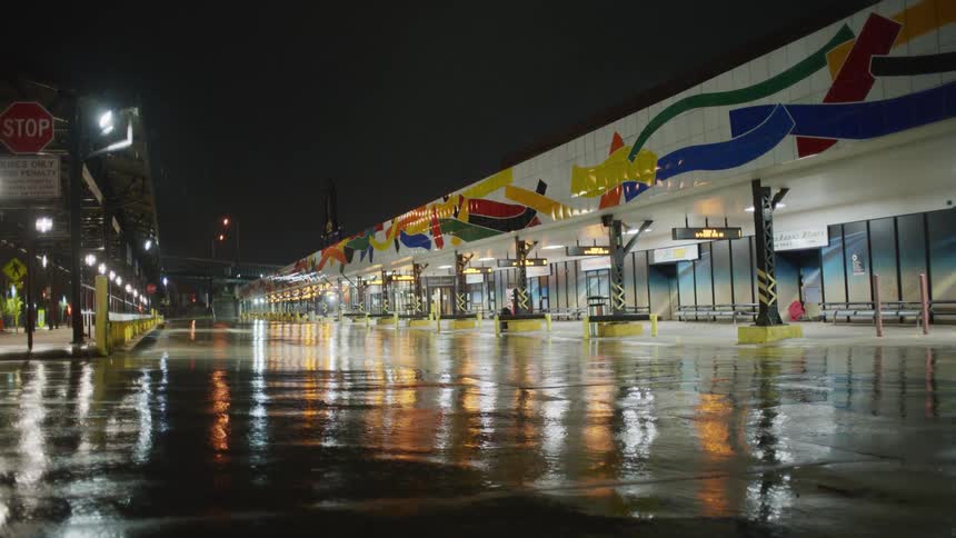 A night time view of a storefronts in an empty plaza area with wet reflecting streets