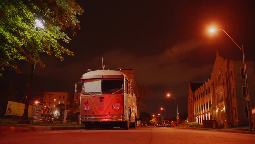An old fashioned bus parked on the side of the road in a city at night