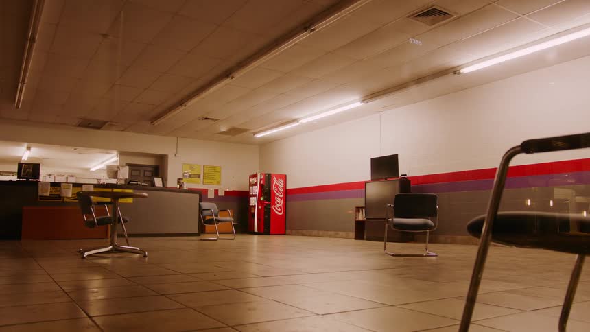 Chairs are spread far apart in an empty group therapy room with an old large screen television and soda vending machine
