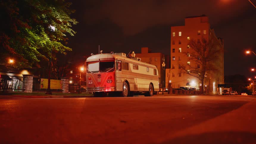 An old fashioned bus parked on the side of the road in a metropolis at night