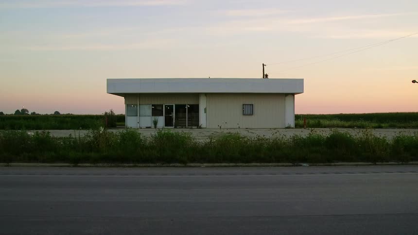 A small building on the side of a road in the countryside in the evening