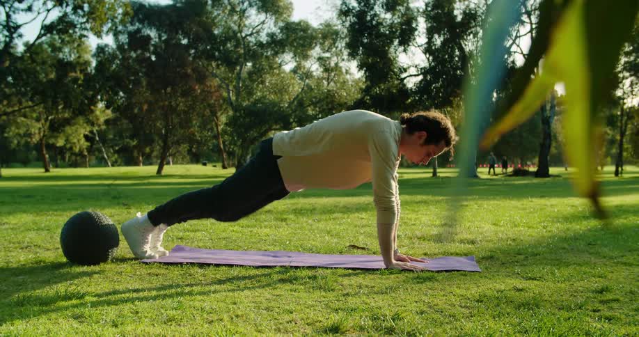 A man does push ups on a yoga mat outside at a public park