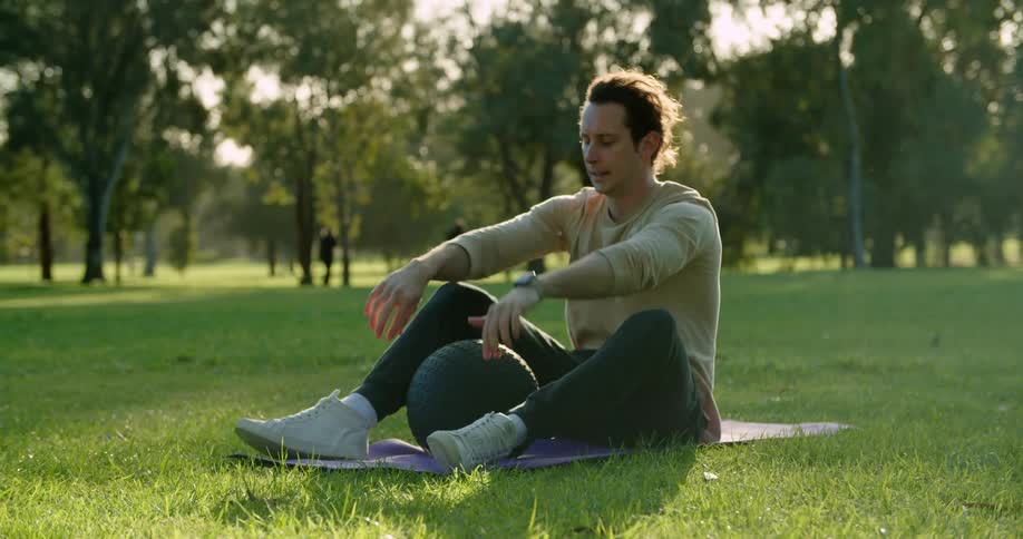 A man in a park exercises while people in the background walk their dog