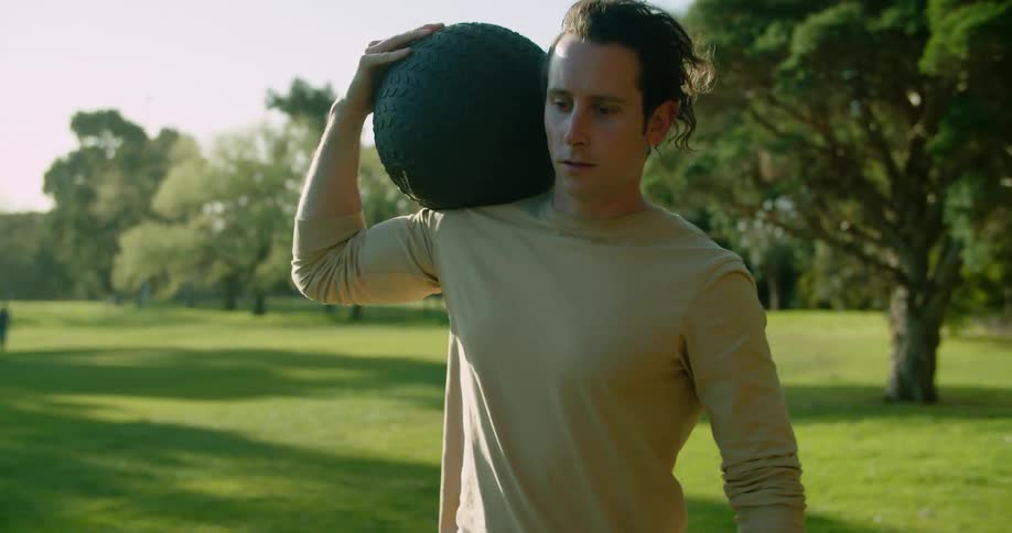 A man in a public park carries a weighted ball as he exercises
