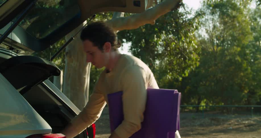 A man opens the back of his car and takes out exercise equipment