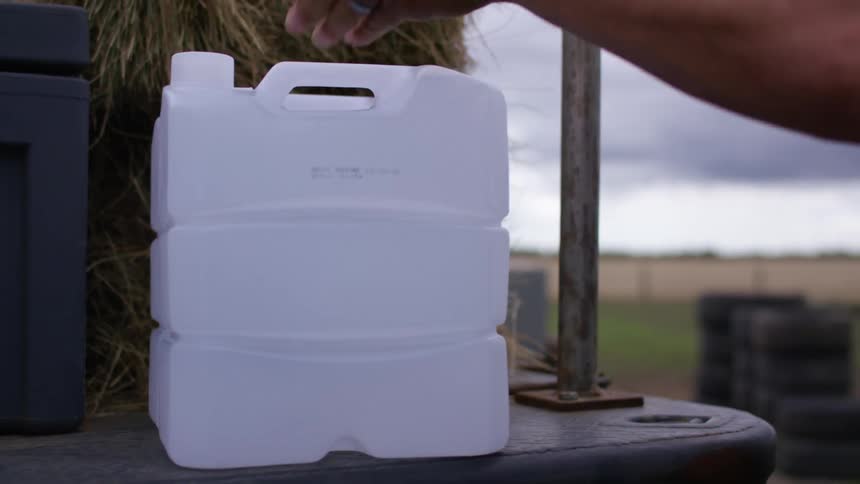A man on a farm unloads jugs onto a platform with bales of hay