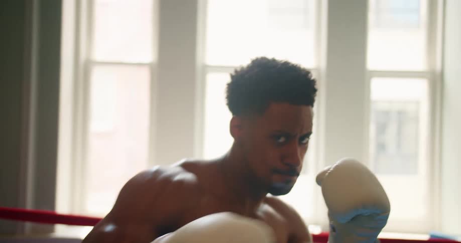 Muscular boxer looks at the camera and throws punches in the boxing ring