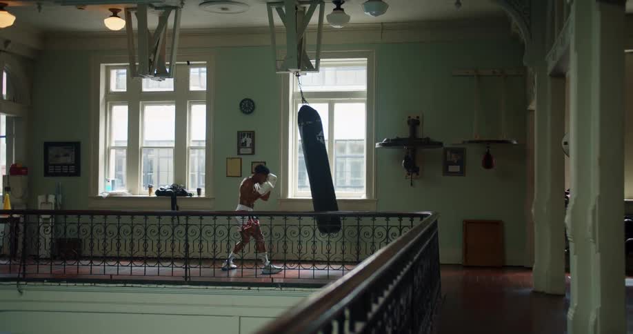 A man punches a punching bag hanging inside beside an upper floor railing