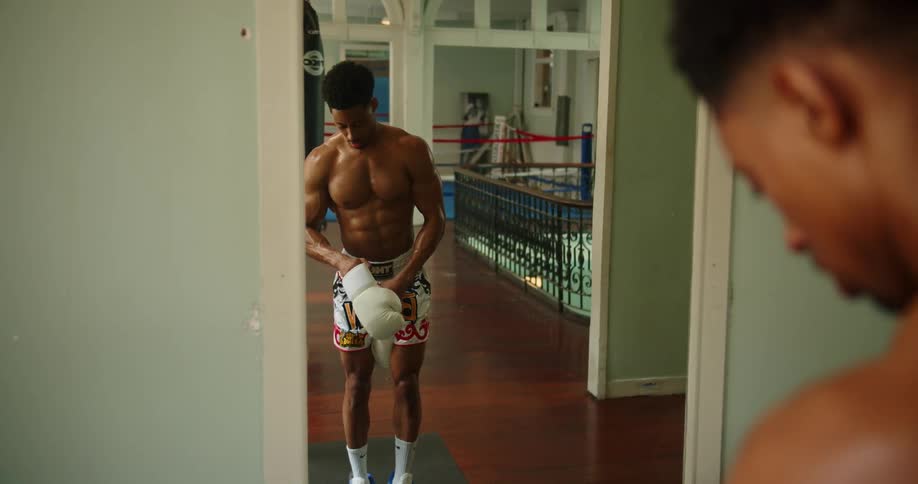 Muscular boxer looks in the mirror and wears a white boxing glove in the gym