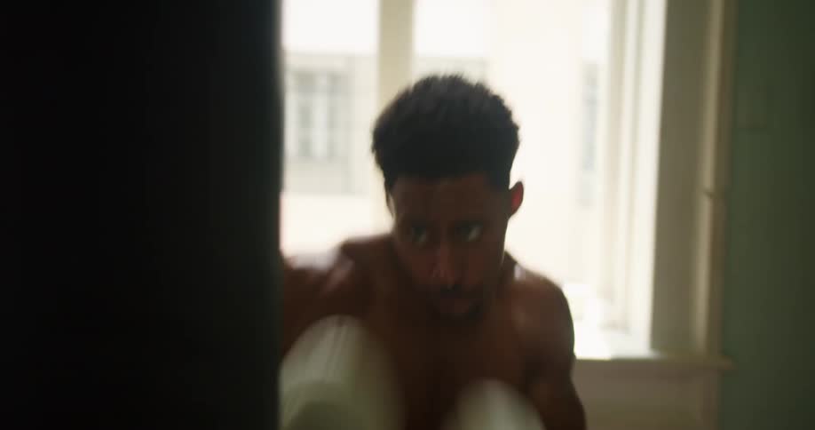 A man with boxing gloves punching a heavy bag with windows in the background