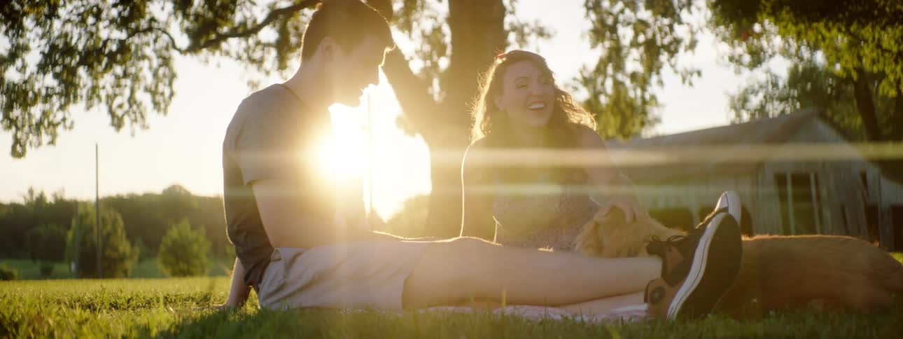 A man and woman sit in a yard petting their dog
