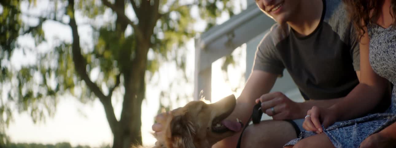 A man and woman sit outside a home petting a dog