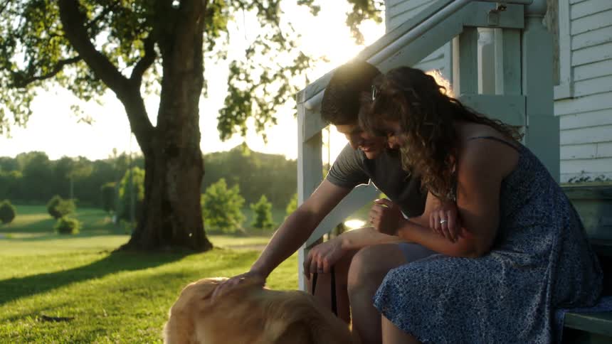 A man and woman sitting on a porch pet their dog