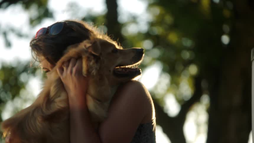 Woman with brown wavy hair cuddles and rubs a golden retriever