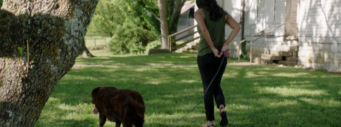 Woman walks dog on leash through yard