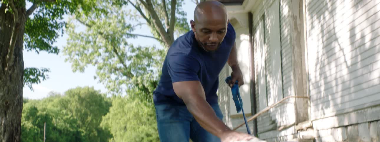 A black man walks and pets a dog outside a house