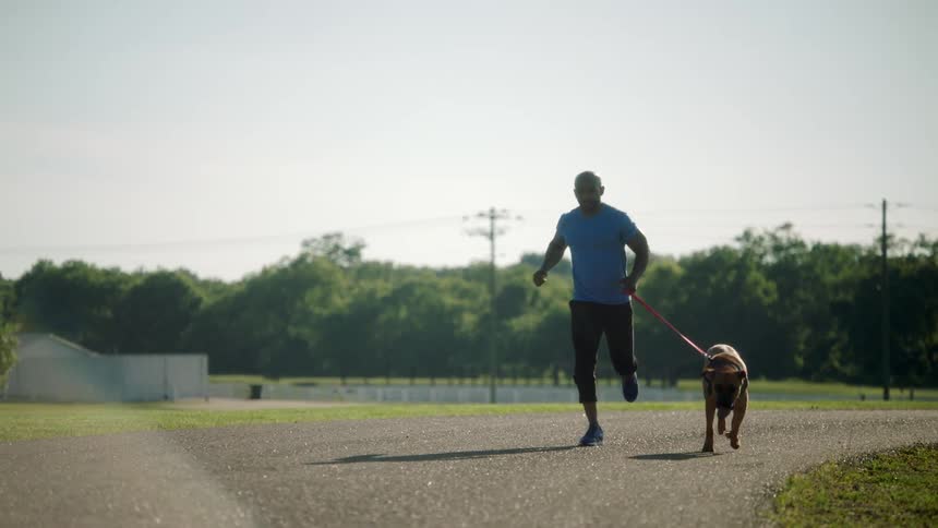 A man runs on a gravel roadway with his dog