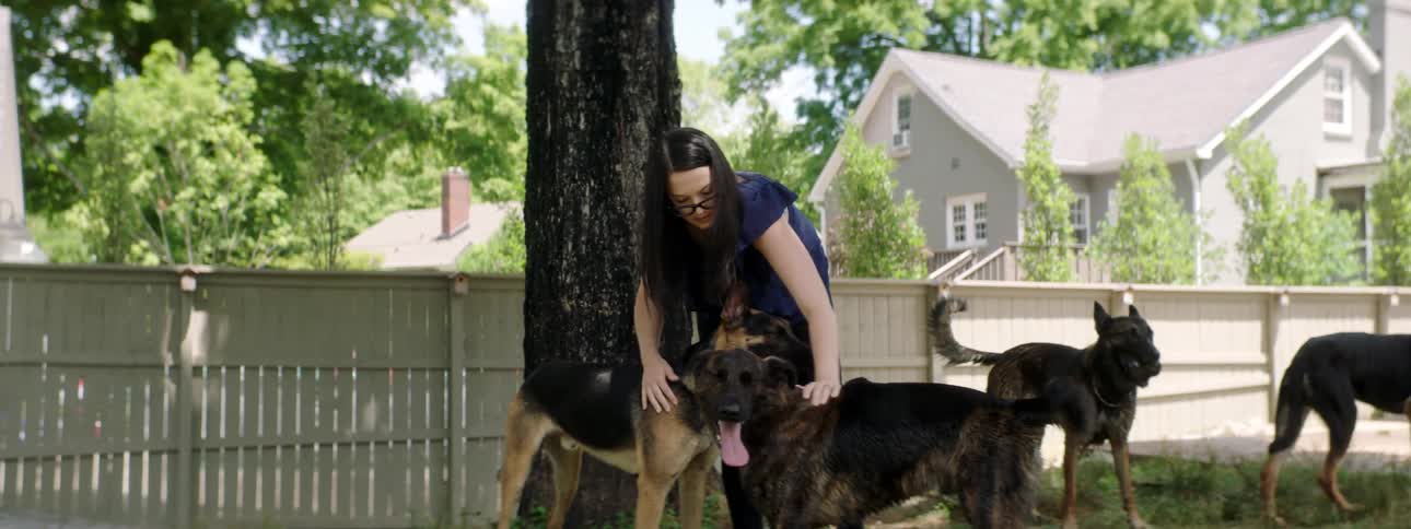 Young woman petting dogs in the lawn on the backyard in a suburban neighborhood