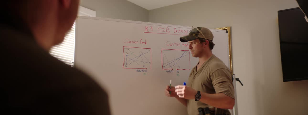 Man wearing military uniform explains a training exercise on a whiteboard in a room