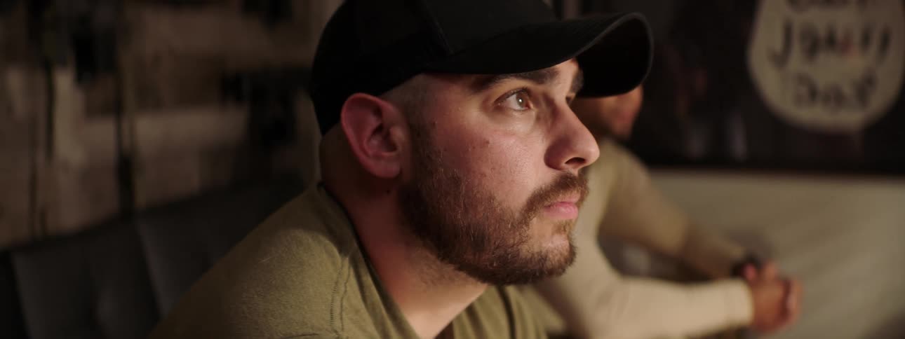 Two men sit inside a house and listen to someone and one man nods his head