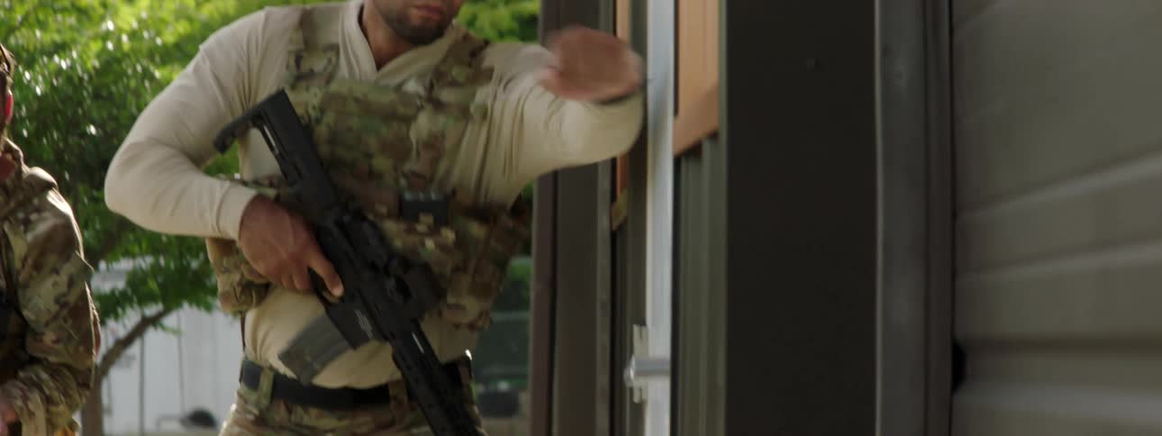 Two military officers knock on a home with large weapons drawn
