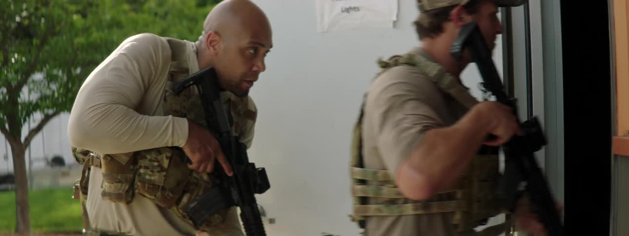 Military men and their dog walk into a building with weapons drawn