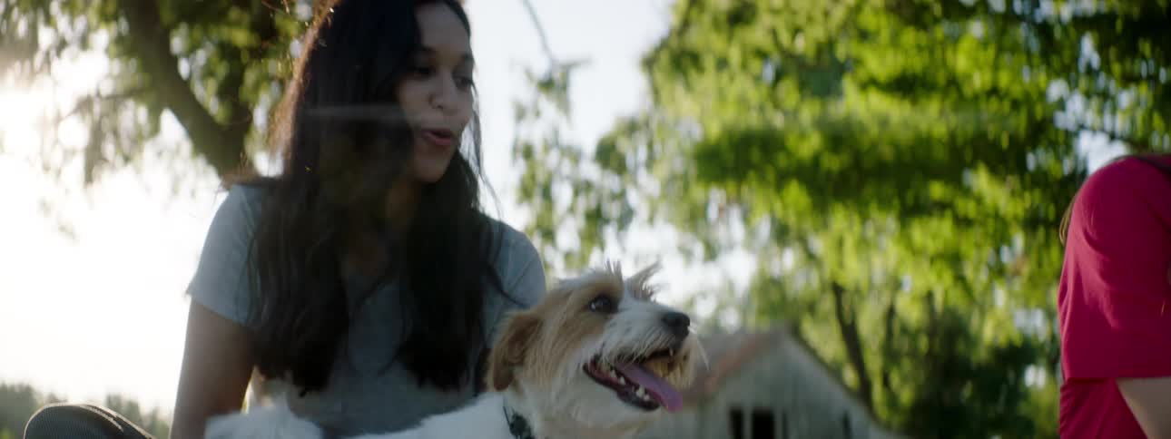 Two women sit outside an old building while one pets a dog