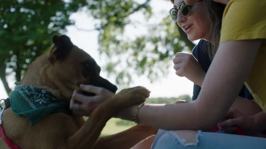Young women sitting outdoors petting dog wearing bandanna