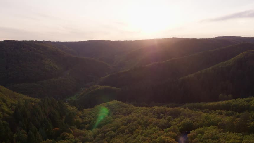 Light from the low sun shines on a mountain range and valley covered in thick forest