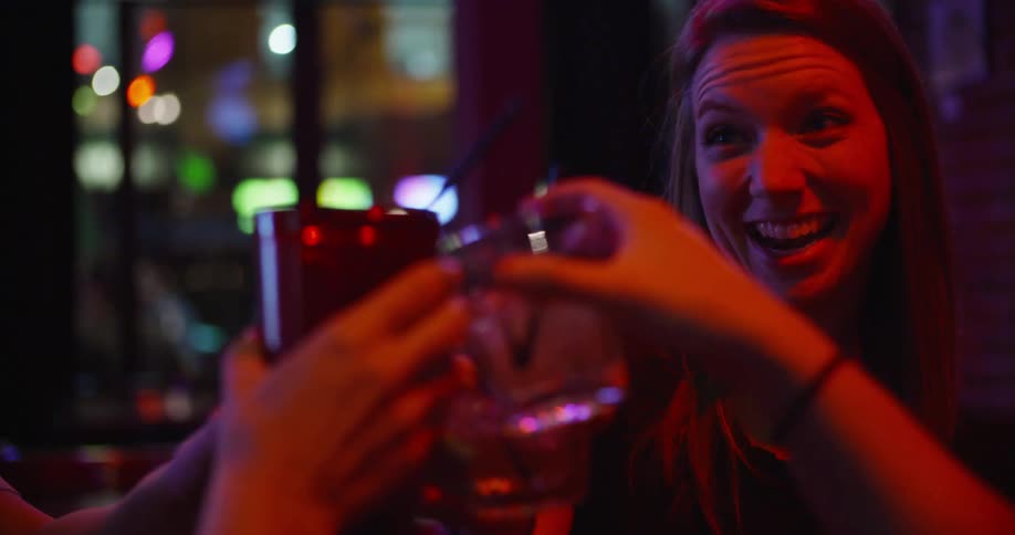 A group of women perform a toast with their drinks in a dimly lit bar